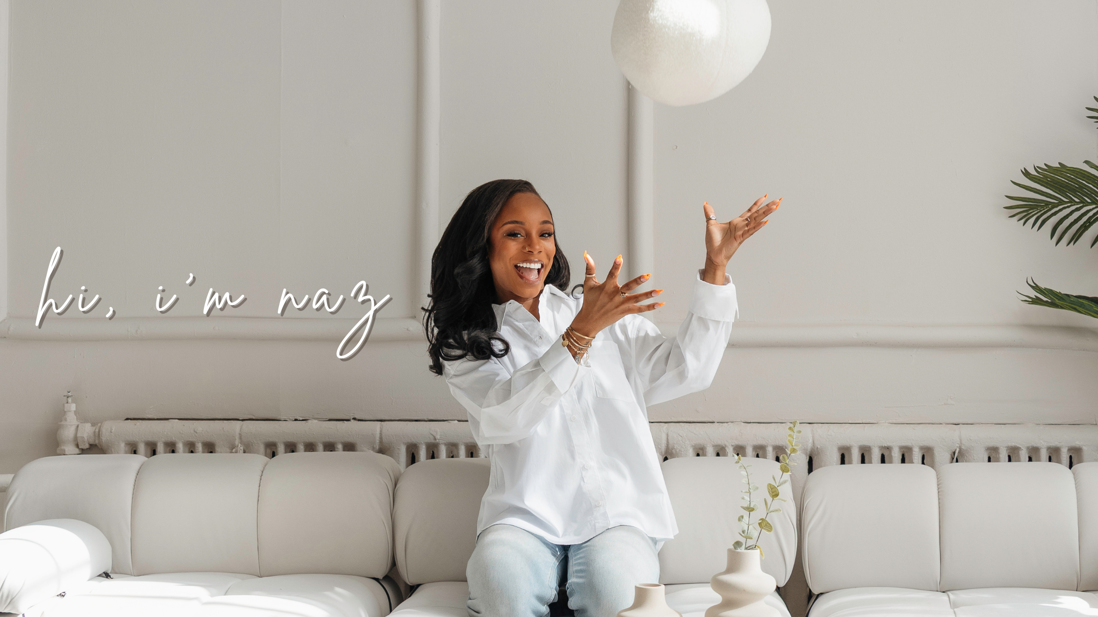 picture of naz, smiling, throwing a pillow up in the air while sitting on a couch. text that reads "hi, im naz"